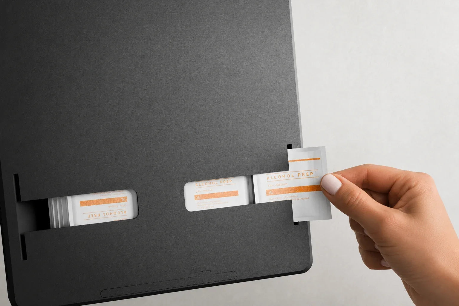 Hand pulling a wrapped prep pad from the built-in dispenser on the underside of the Routine Box