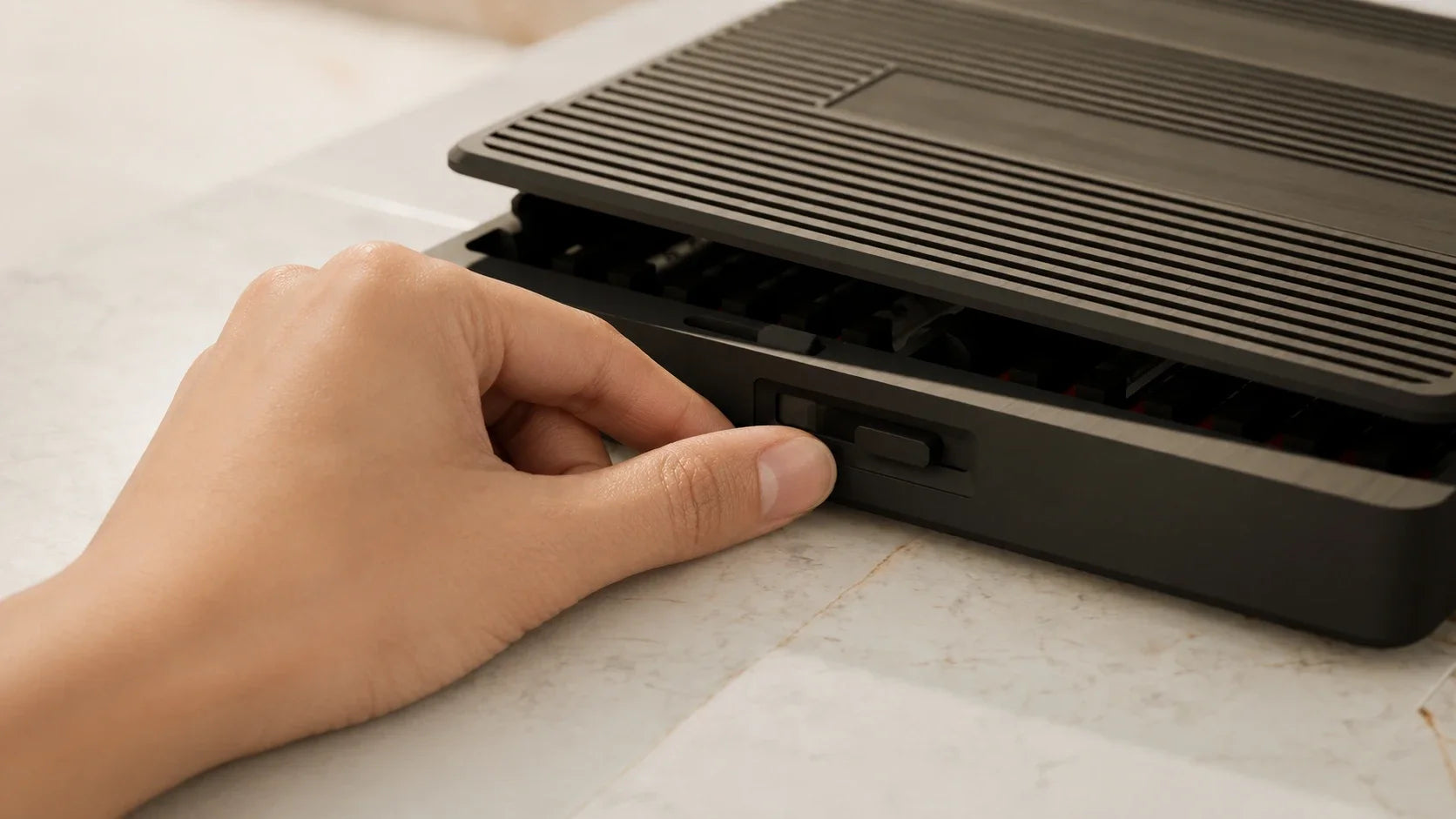 A thumb sliding open the front latch of the Routine Box